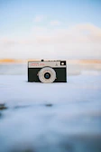 A close-up of a vintage film camera set against the snowy Shimla backdrop.