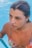 A person is emerging from a swimming pool, water droplets glistening on their skin. They are wearing a colorful swimsuit with floral patterns. The background consists of clear blue pool water.