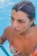 A person is emerging from a swimming pool, water droplets glistening on their skin. They are wearing a colorful swimsuit with floral patterns. The background consists of clear blue pool water.