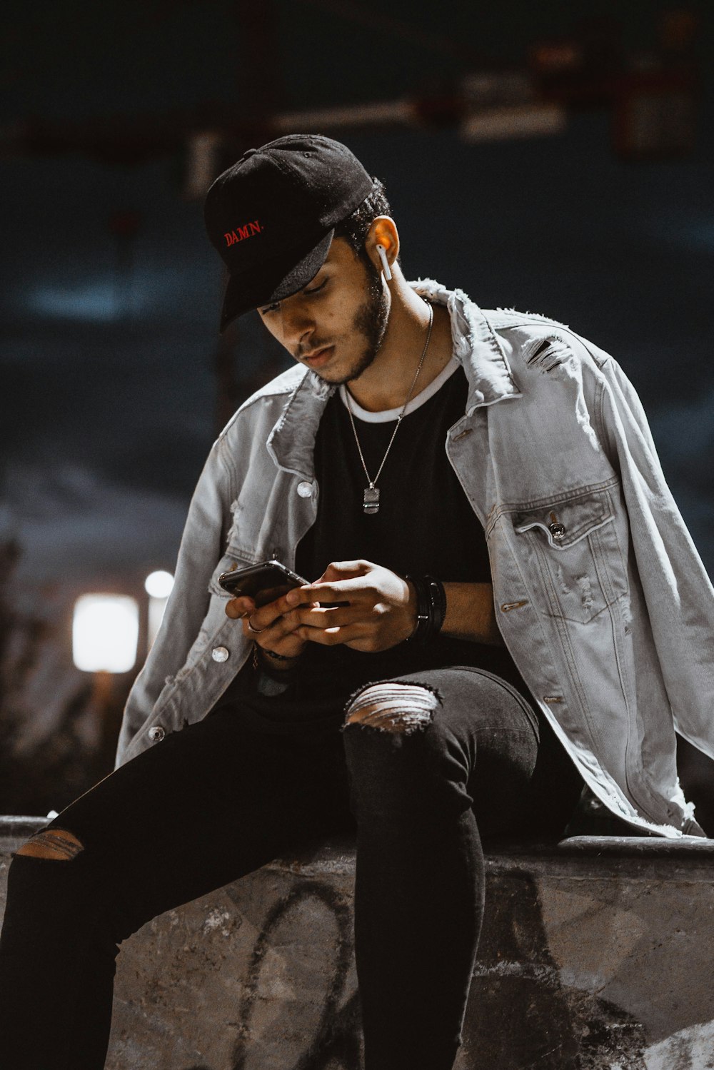 man in gray denim jacket and black knit cap sitting on gray concrete floor