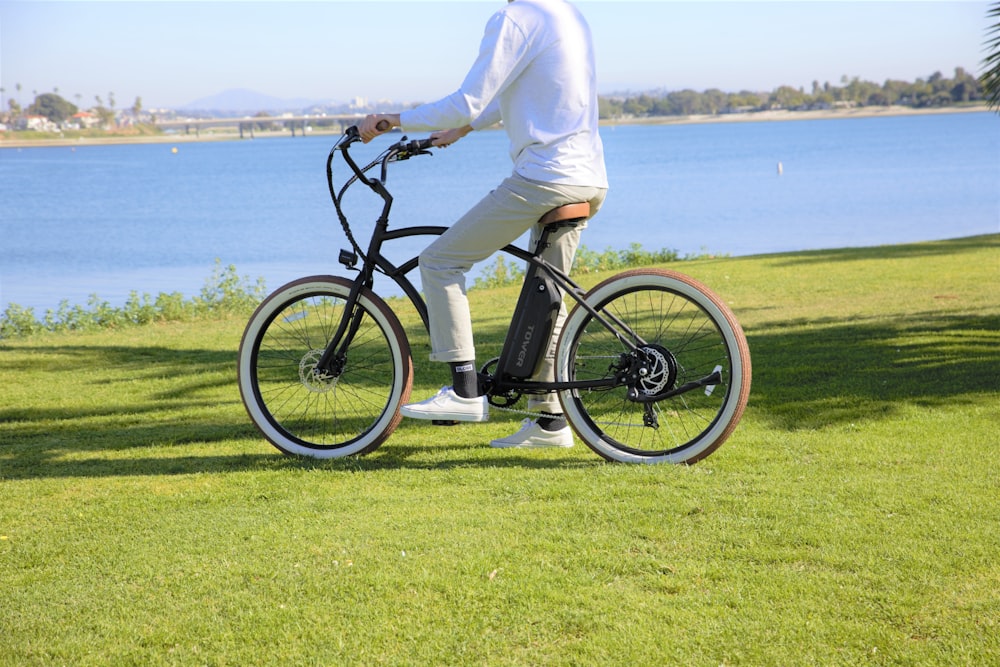 person in white pants and black shirt riding black bicycle on green grass field near body