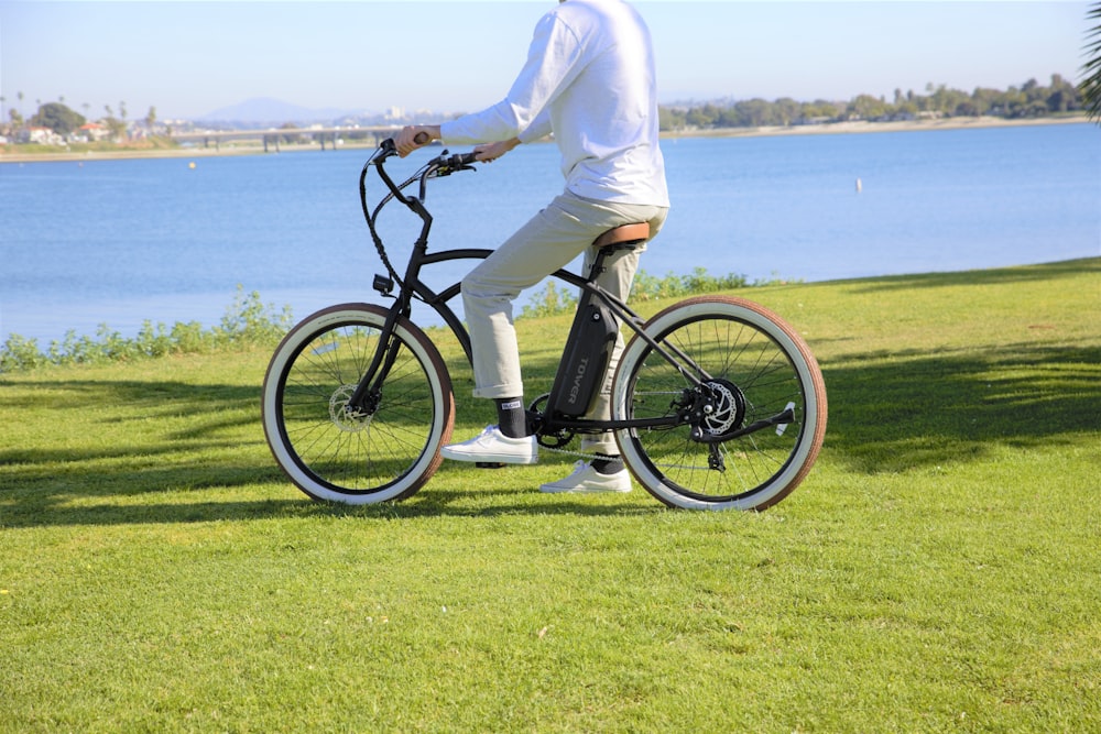 白いズボンと黒いシャツを着た人が、体の近くの緑の芝生で黒い自転車に乗っています