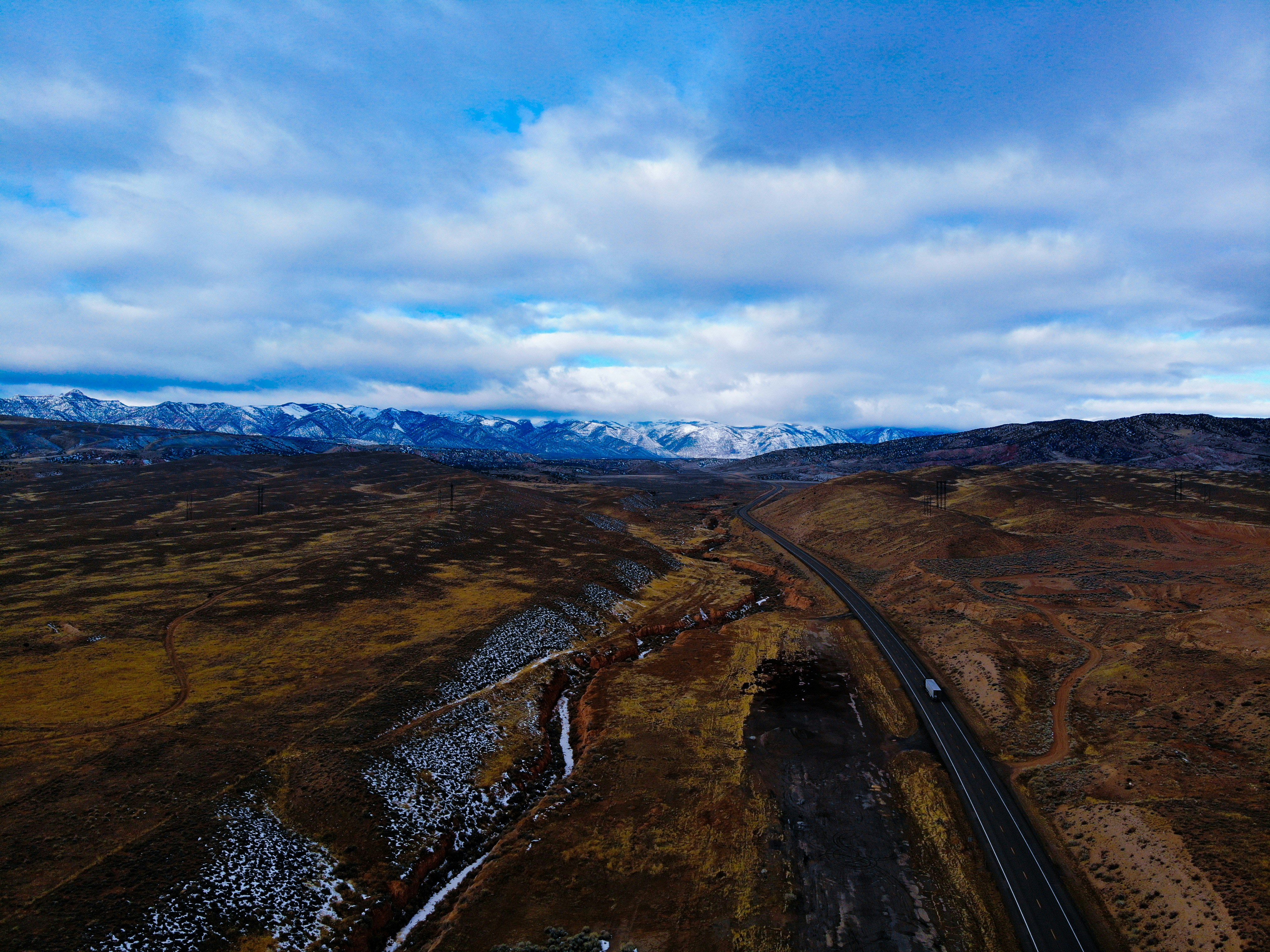 black asphalt road between brown and green mountains under blue and white sunny cloudy sky during