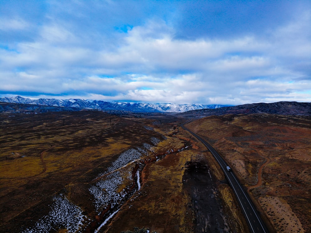 black asphalt road between brown and green mountains under blue and white sunny cloudy sky during