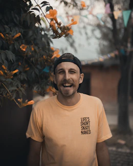 man in white crew neck t-shirt standing near brown leaves during daytime