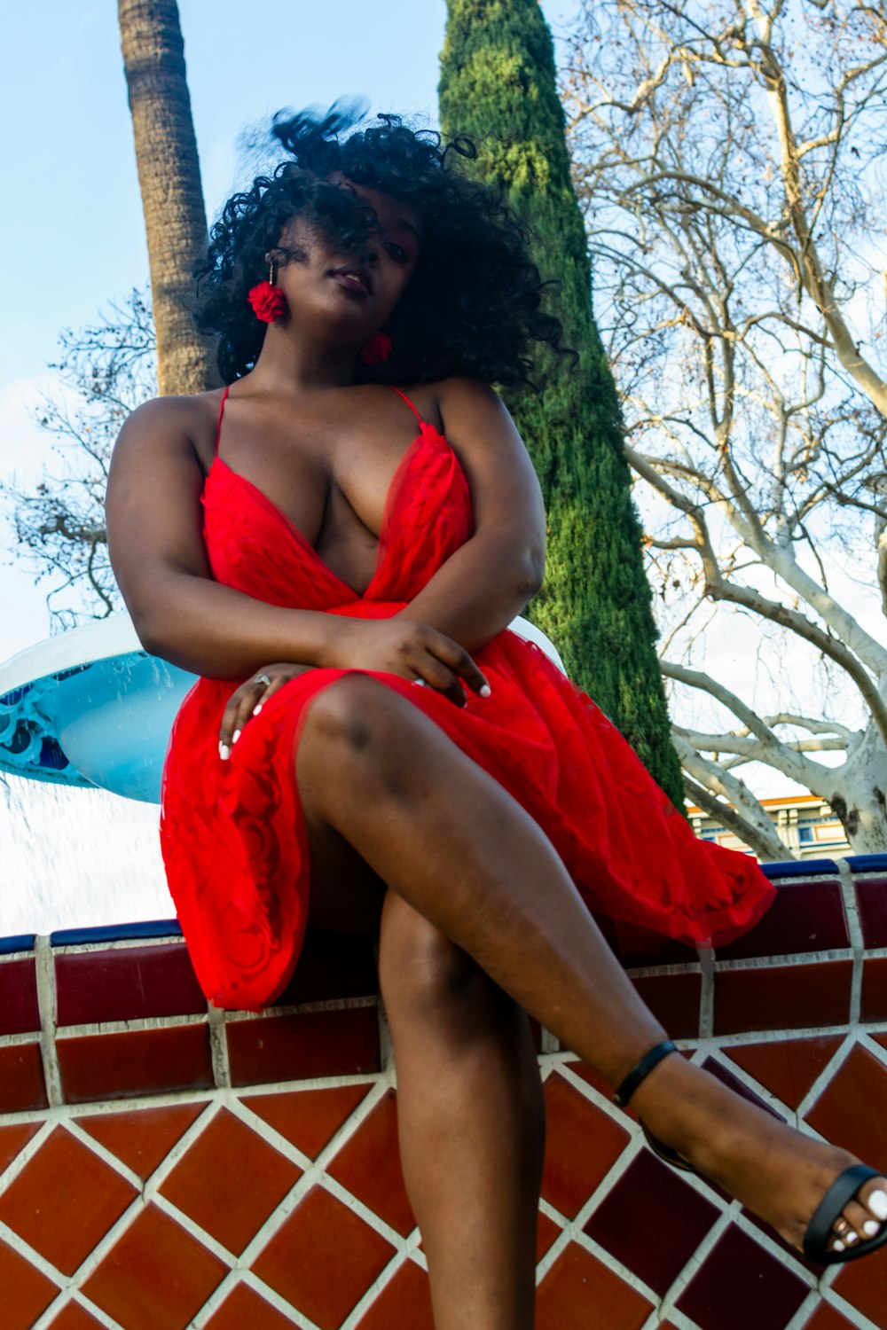 woman in red spaghetti strap top sitting on blue and red textile