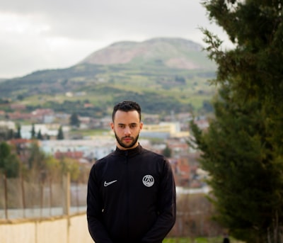 man in black hoodie standing near green trees during daytime algeria teams background