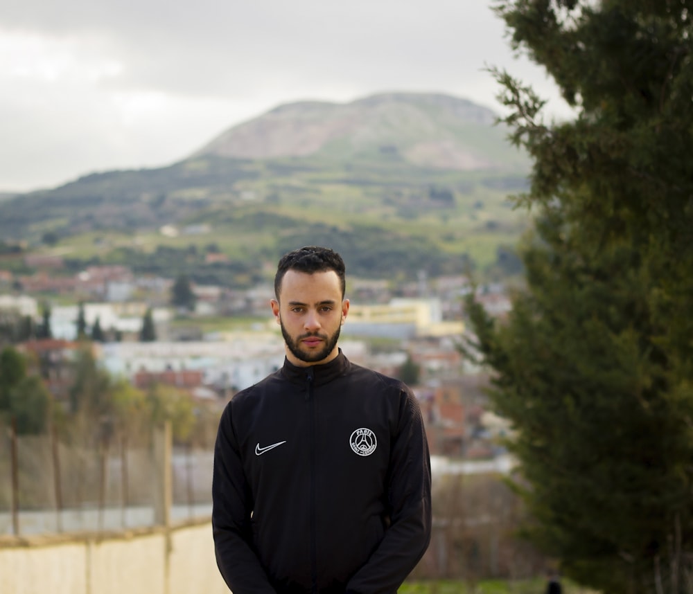 man in black hoodie standing near green trees during daytime