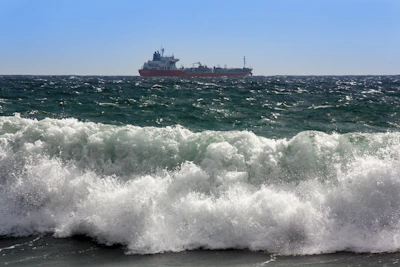 A dynamic cargo ship cutting through ocean waves under a bright sky.