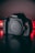 A Canon EOS Rebel T3i camera is positioned on a reflective surface with a low-key lighting setup. The background is dimly lit with a strip of red lights, giving a dramatic contrast.