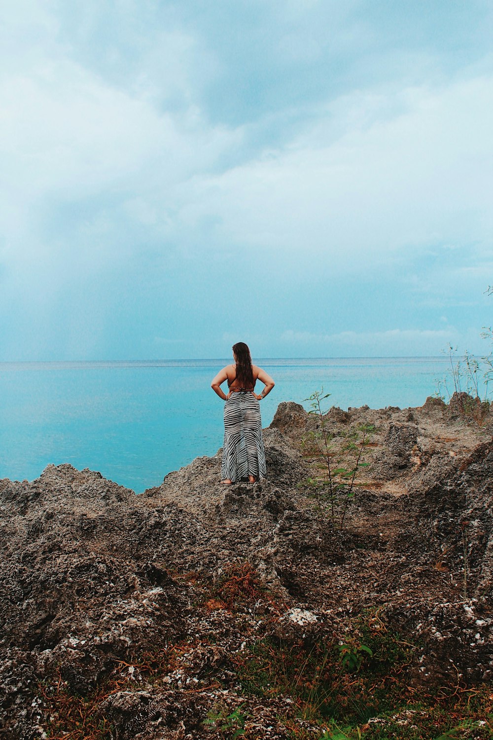 woman in white and black dress standing on brown rock near body of water during daytime