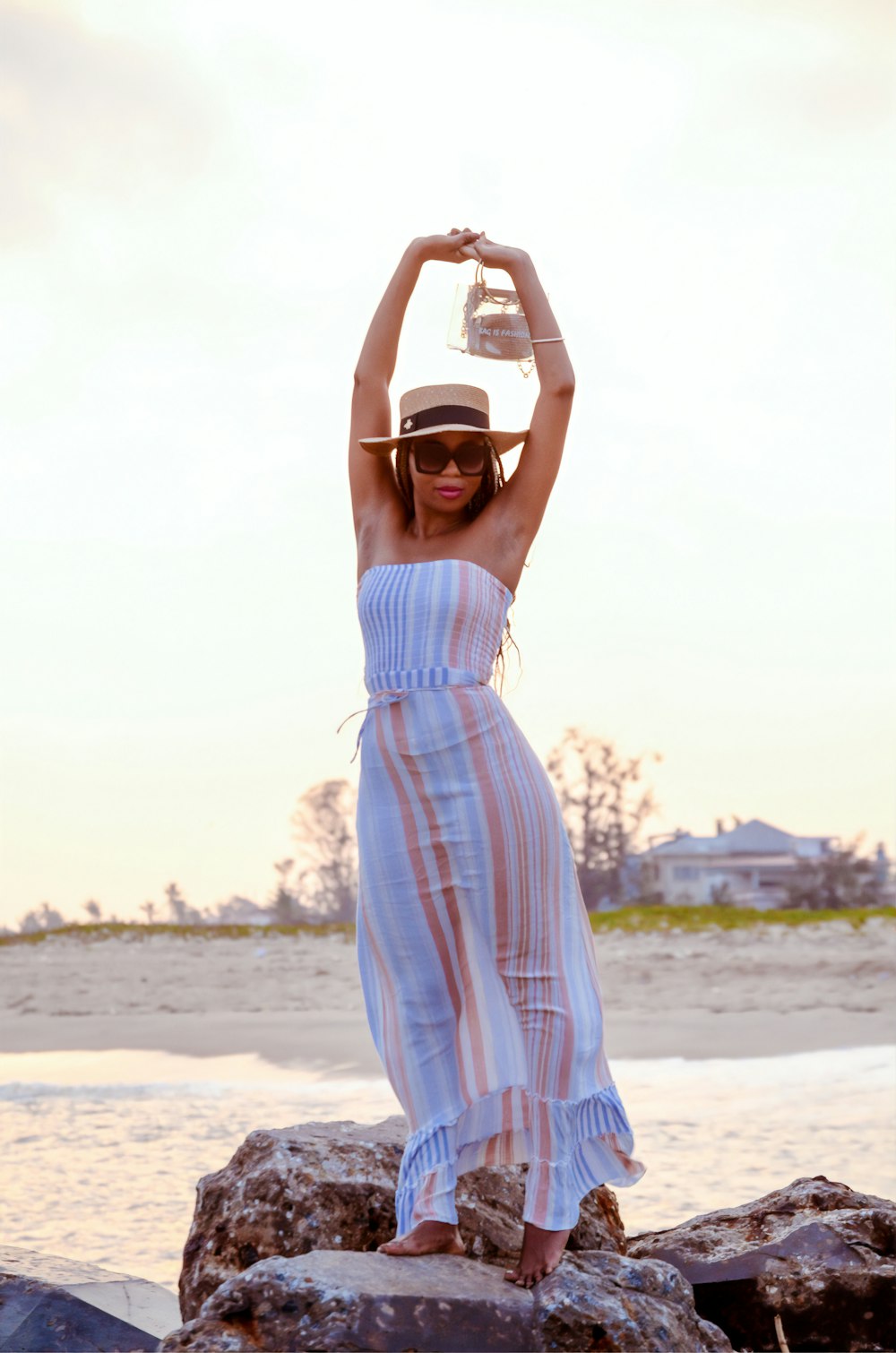 낮 동안 해변에 서 있는 흰색 선글라스를 쓴 흰색과 분홍색 줄무늬 드레스를 입은 여자