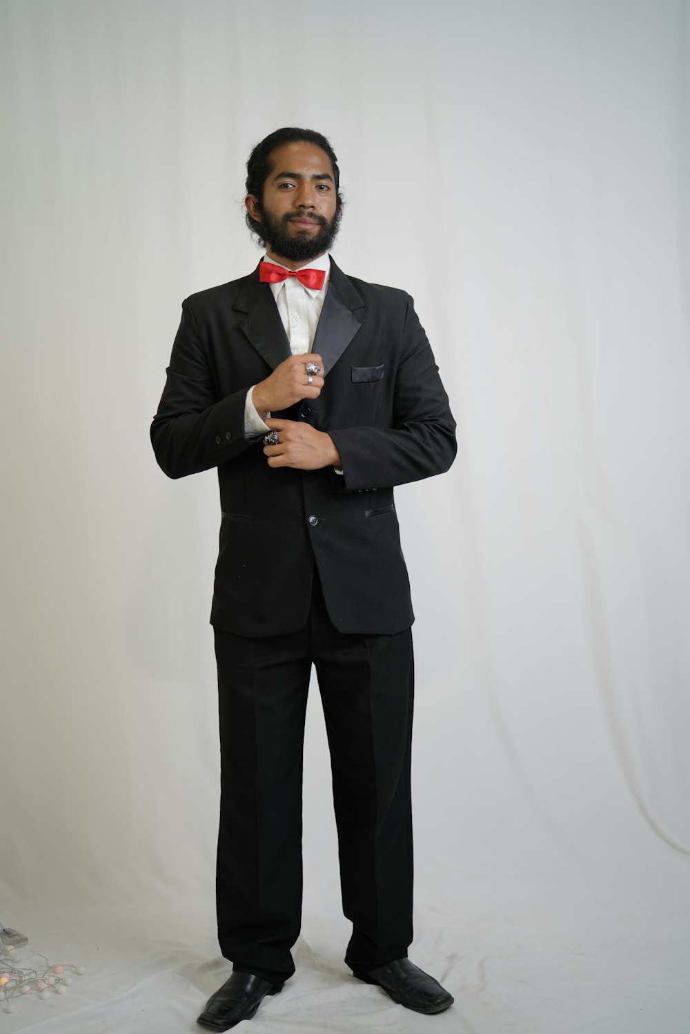 man in black suit standing beside white wall