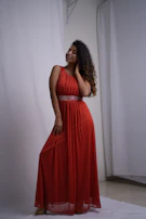 An elegant model posing gracefully in a sleek black dress illuminated by soft red lighting.