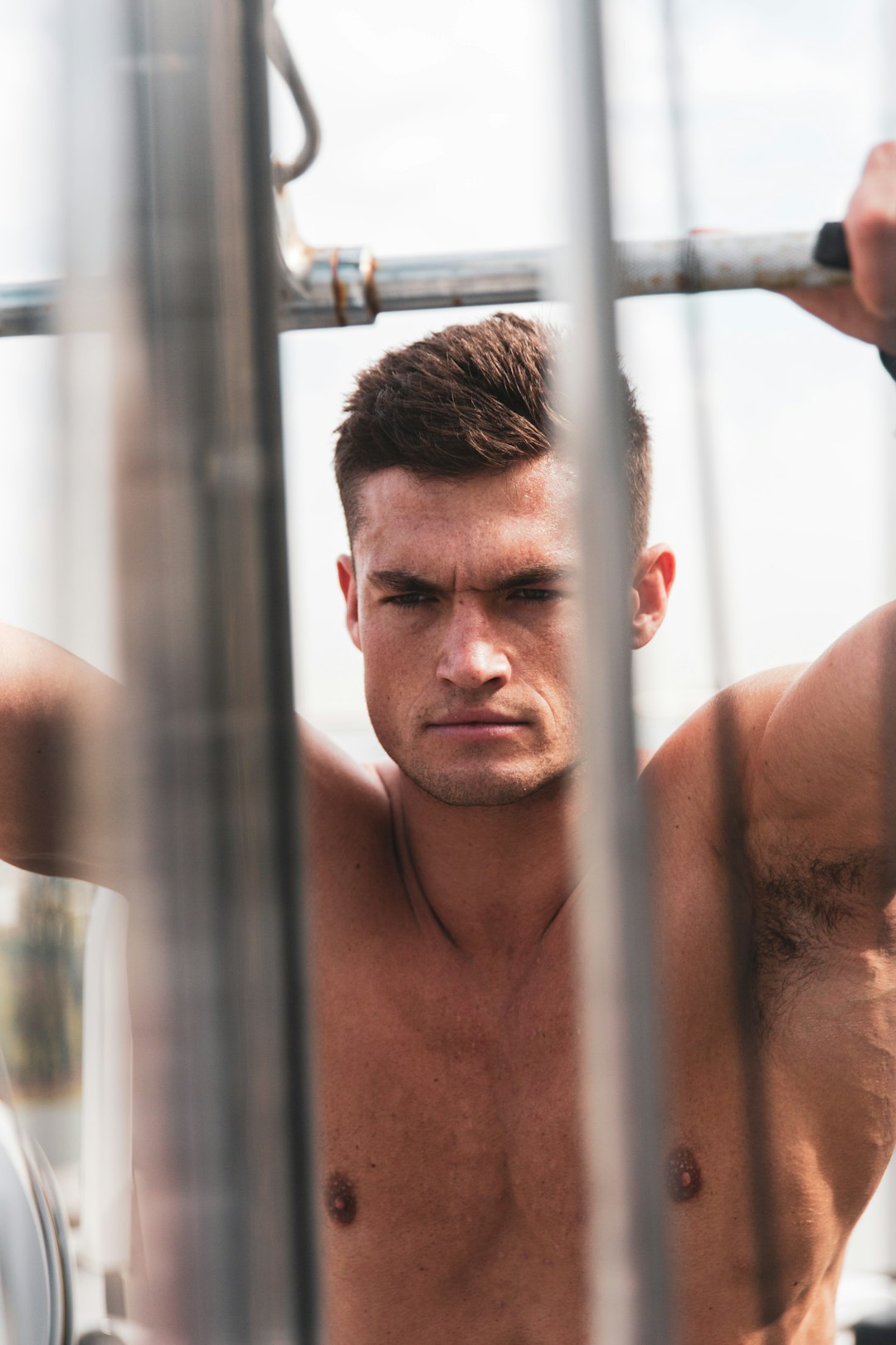 topless man leaning on gray metal bar