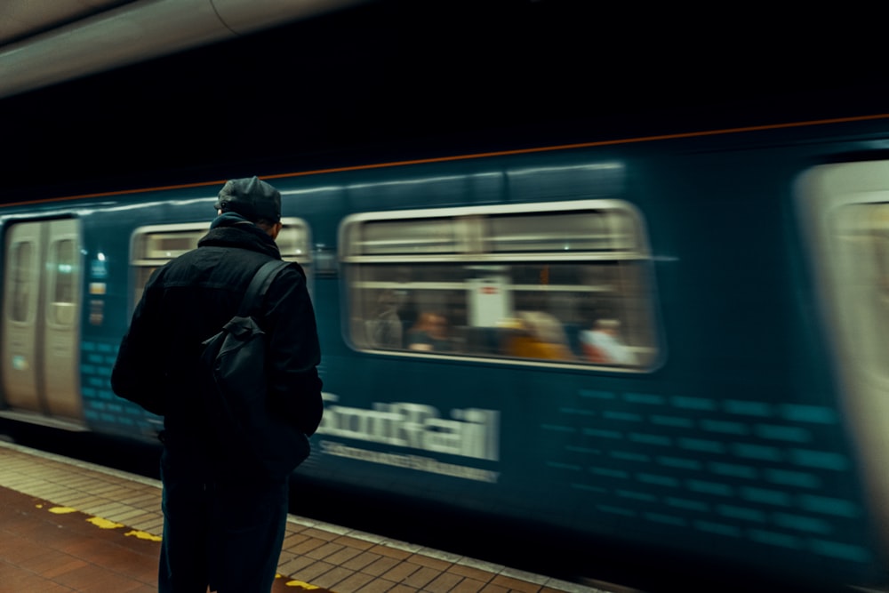 man in black jacket standing beside blue and white train