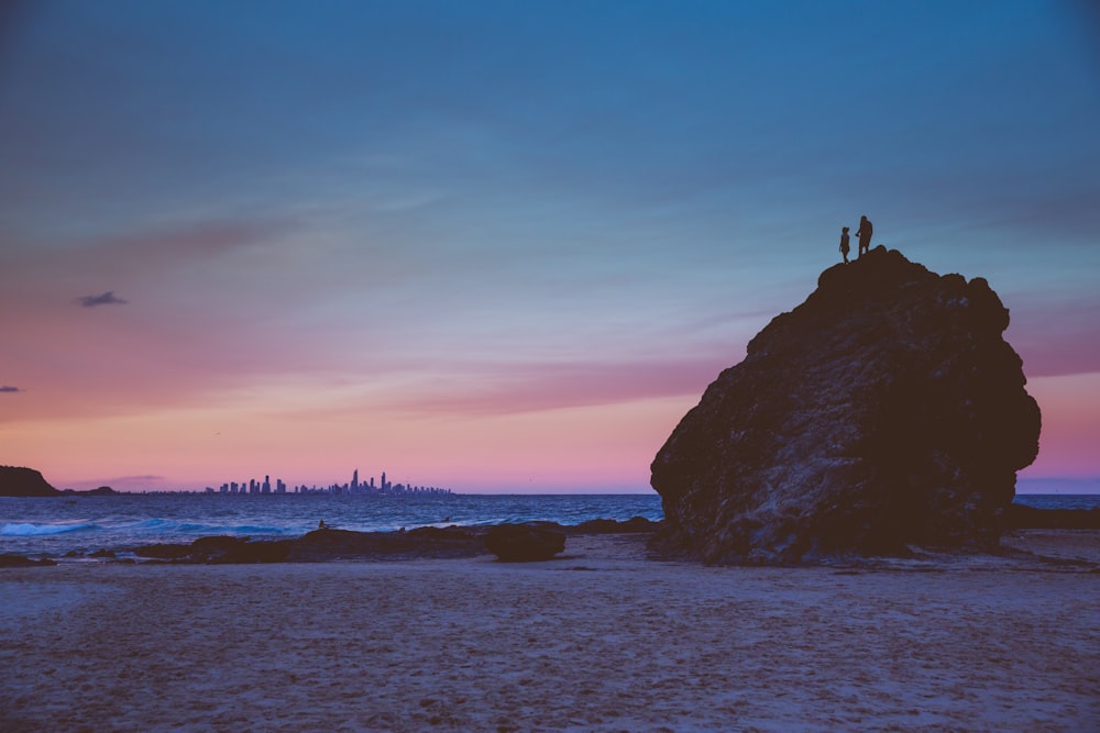 silhouette of person standing on rock formation during sunset