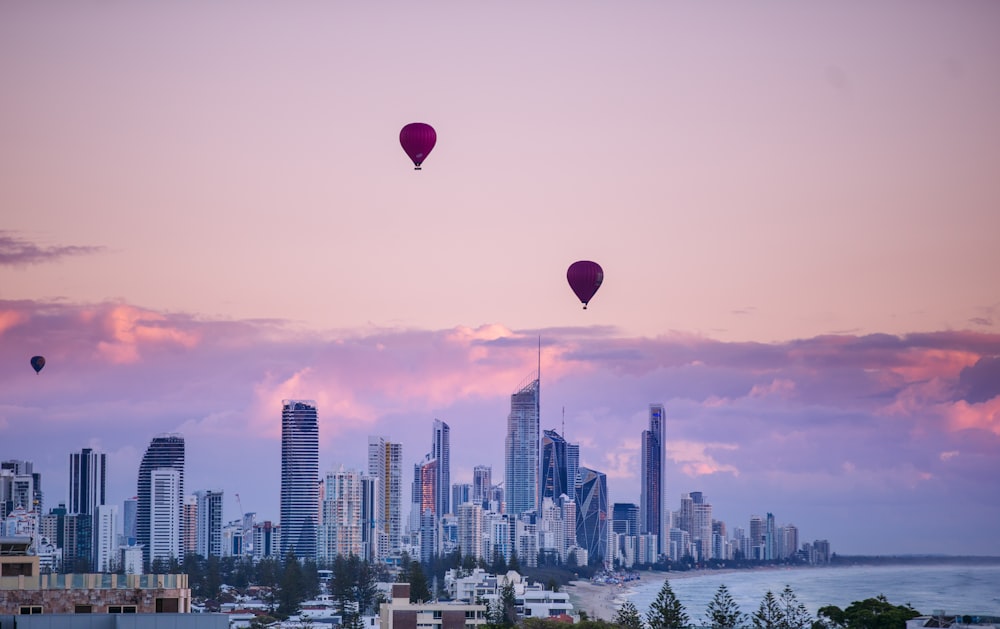 balões de ar quente vermelhos e azuis sobre o horizonte da cidade durante o pôr do sol