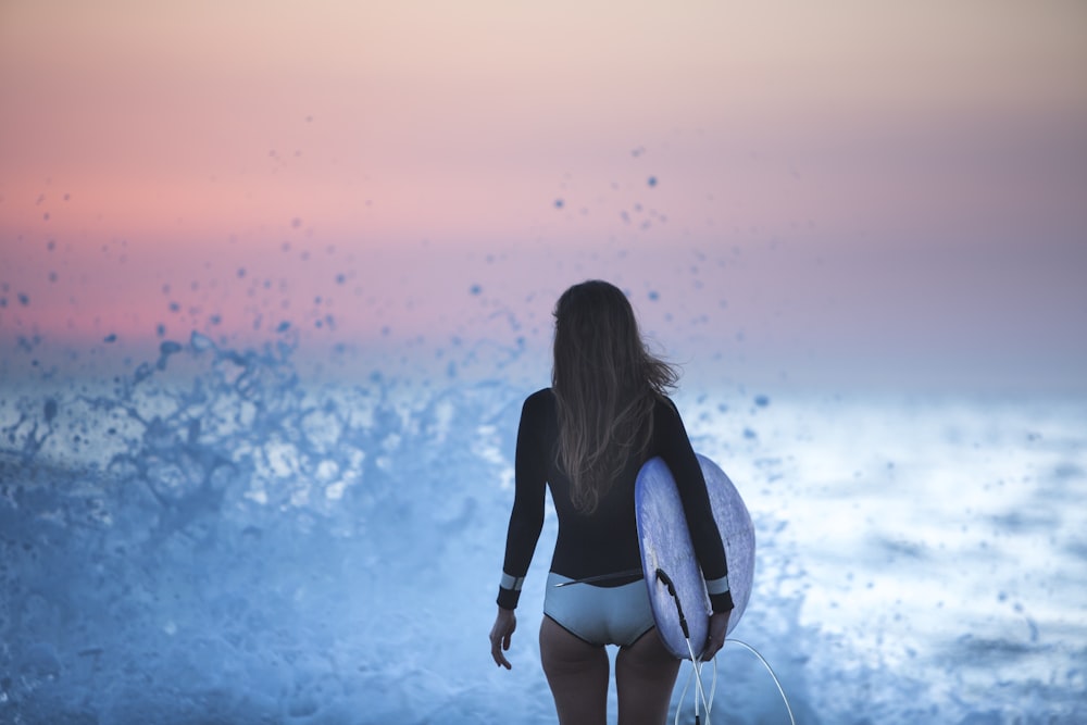 mulher na camisa preta de manga comprida e shorts brancos em pé na água azul durante o pôr do sol