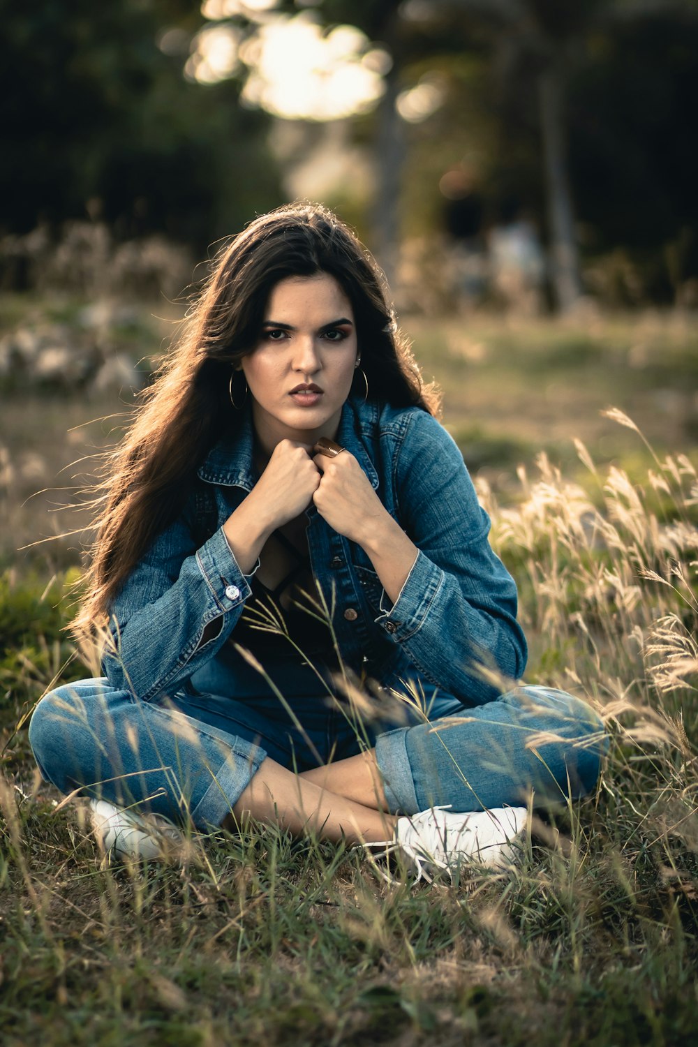 woman in blue denim jacket and blue denim jeans sitting on green grass field during daytime