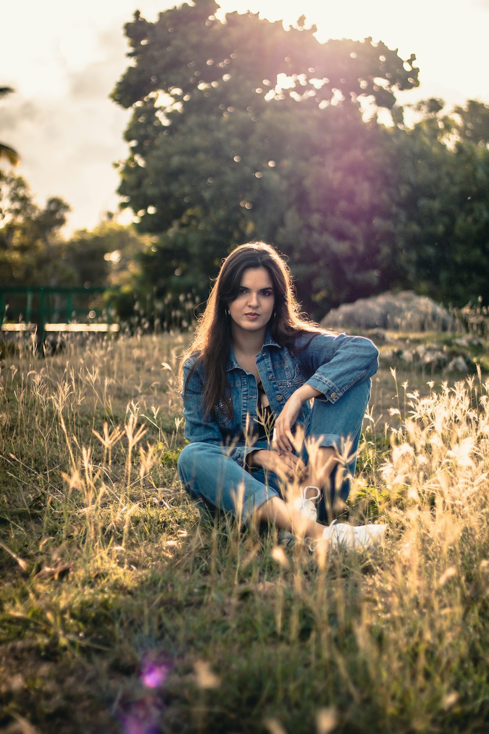 woman in blue denim jacket and blue denim jeans sitting on brown grass field during daytime