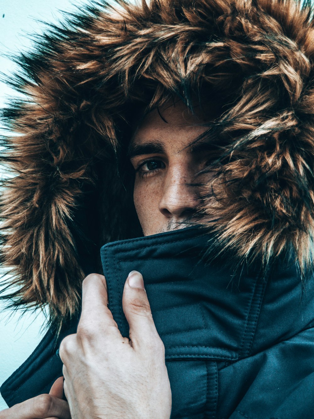 woman in black leather jacket covering her face with black and brown fur scarf