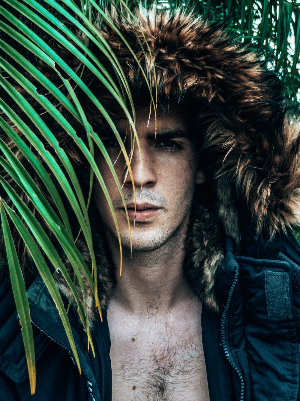 man in black leather jacket standing beside green palm plant