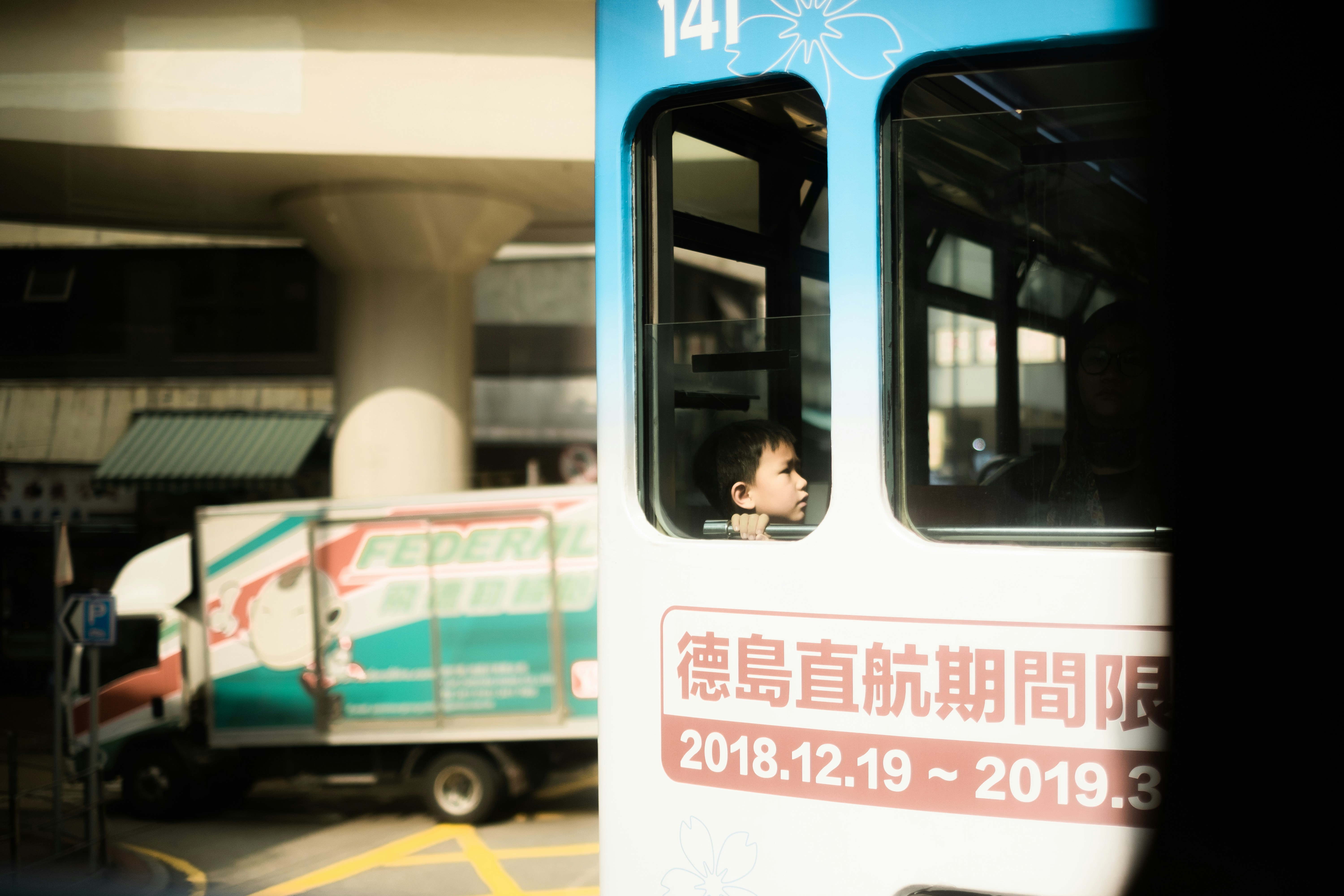 Mann in schwarzer Jacke tagsüber neben blau-weißem Bus