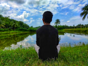 man in black shirt sitting on grass field near lake during daytime
