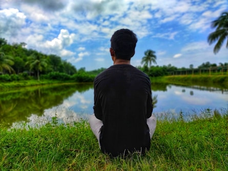 man in black shirt sitting on grass field near lake during daytime