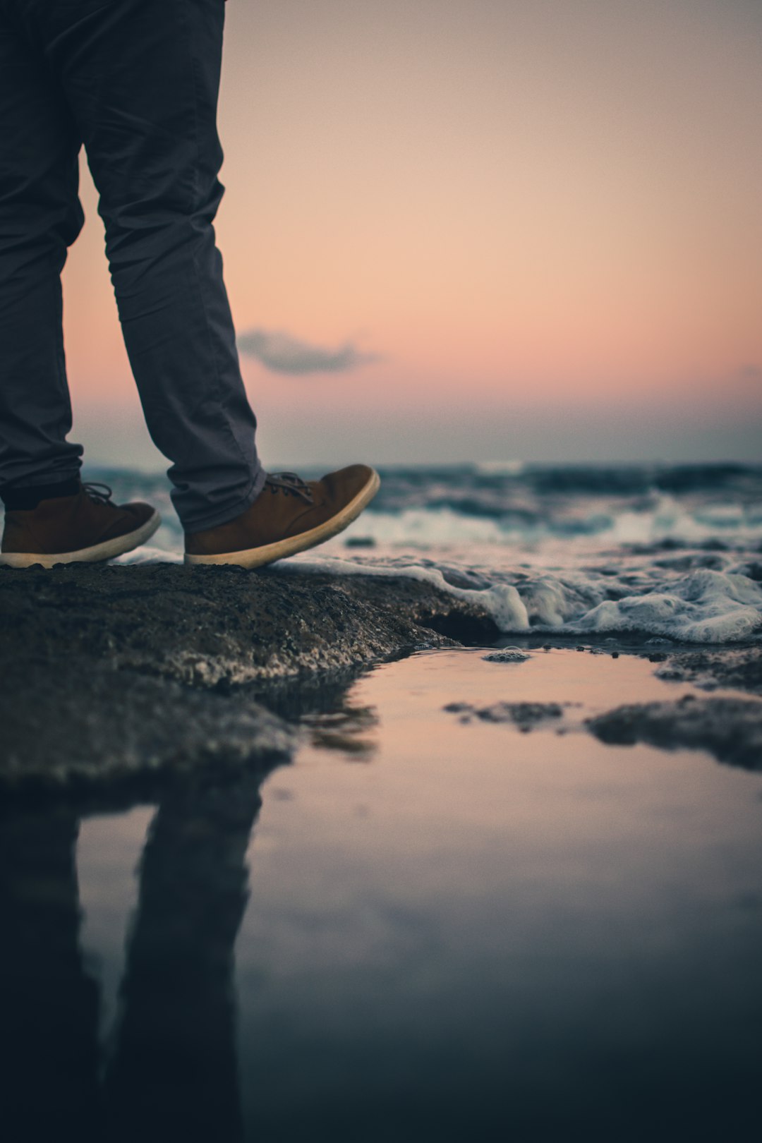 person in blue denim jeans and brown shoes standing on rocky shore during daytime