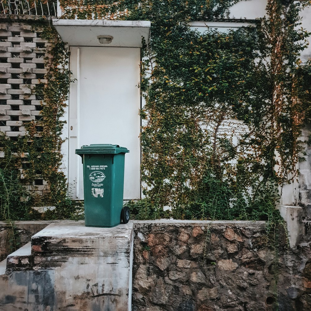 green trash bin beside concrete wall