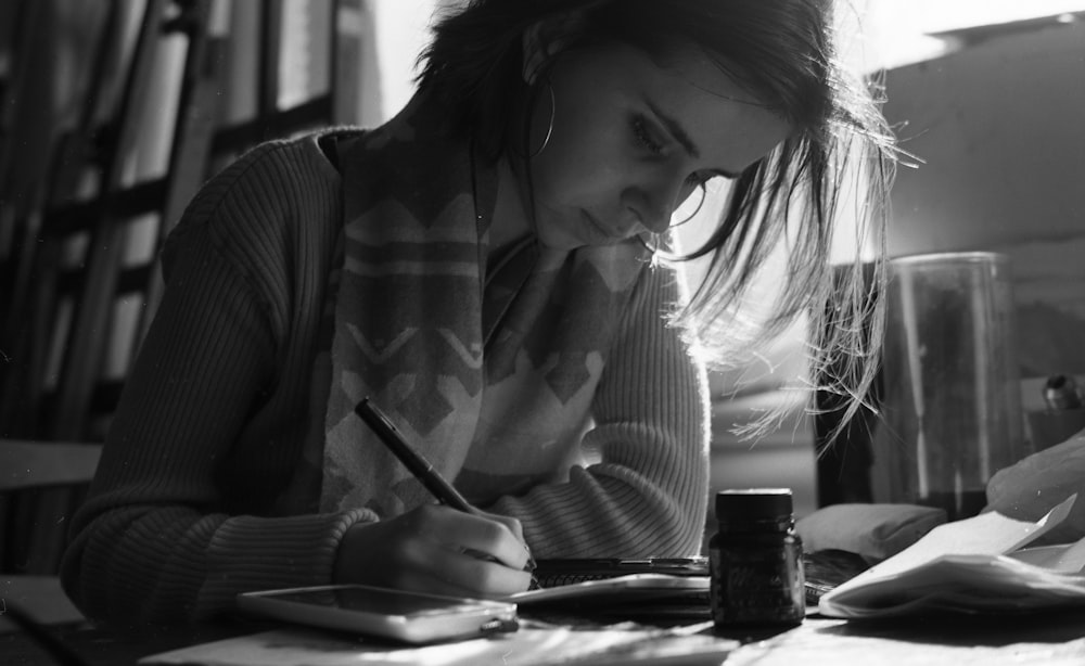 a woman sitting at a table writing on a piece of paper