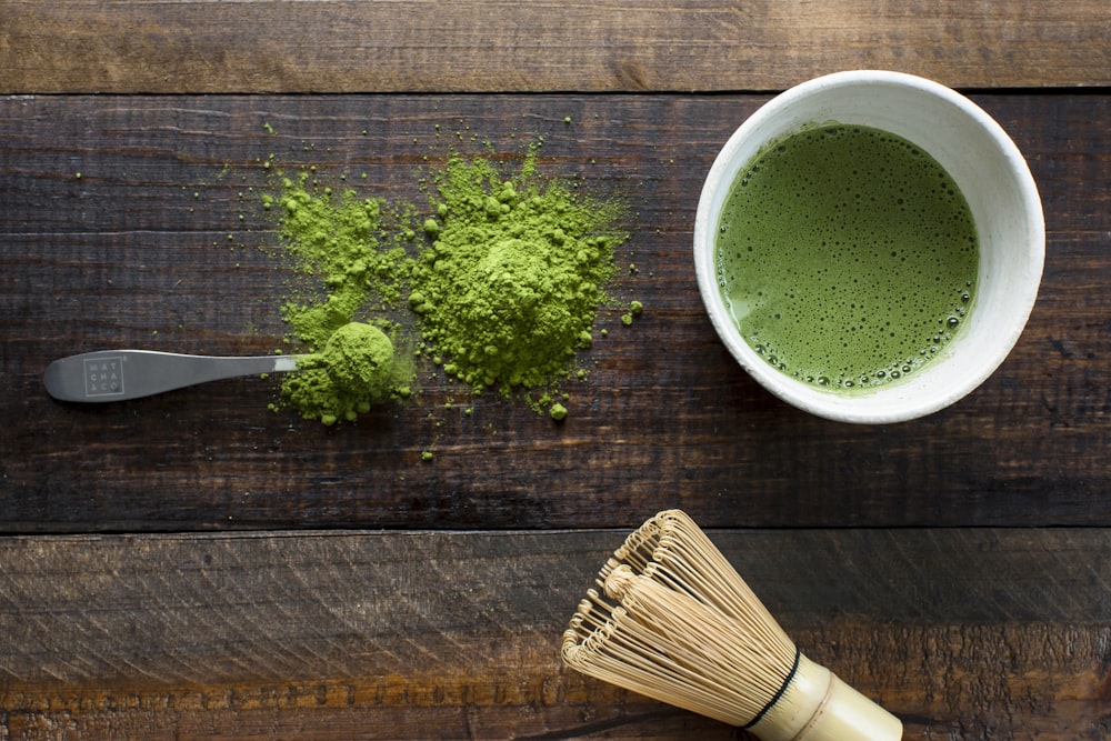 茶色の木製のブラシの横の白いセラミックマグカップの緑の植物