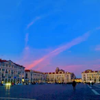 Artistic rendering of a lively town plaza bathed in warm tropical sunlight with vivid red and yellow tones.