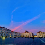 Artistic rendering of a lively town plaza bathed in warm tropical sunlight with vivid red and yellow tones.