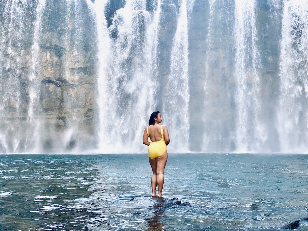 woman in yellow bikini standing on water falls during daytime