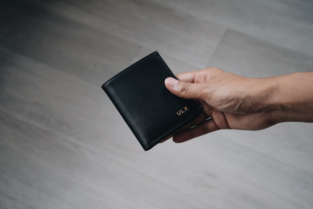 Persona sosteniendo billetera plegable de cuero negro