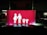 A bright red sign features white pictograms representing a family, consisting of two adults on the left and two children on the right, all holding hands. The scene is set against a dark background, suggesting it might be located in a parking area or similar environment.
