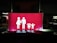 A bright red sign features white pictograms representing a family, consisting of two adults on the left and two children on the right, all holding hands. The scene is set against a dark background, suggesting it might be located in a parking area or similar environment.