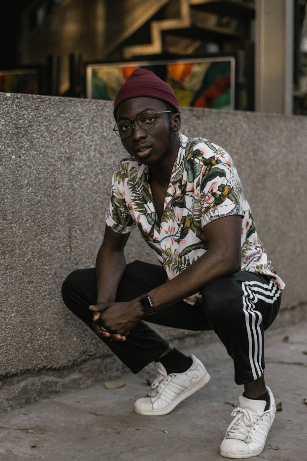 man in white black and yellow floral button up shirt and black pants sitting on gray