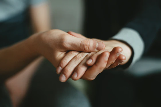 A gentle hand resting on another’s in a hospital room, symbolizing comfort and spiritual support.