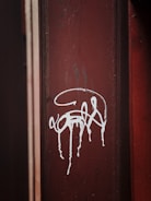 A close-up view of a brown metal surface with white graffiti art that appears to be dripped or splattered.