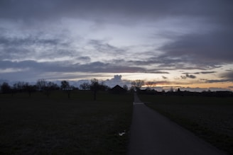 A dramatic landscape of storm clouds rolling over a quiet countryside road at dusk.