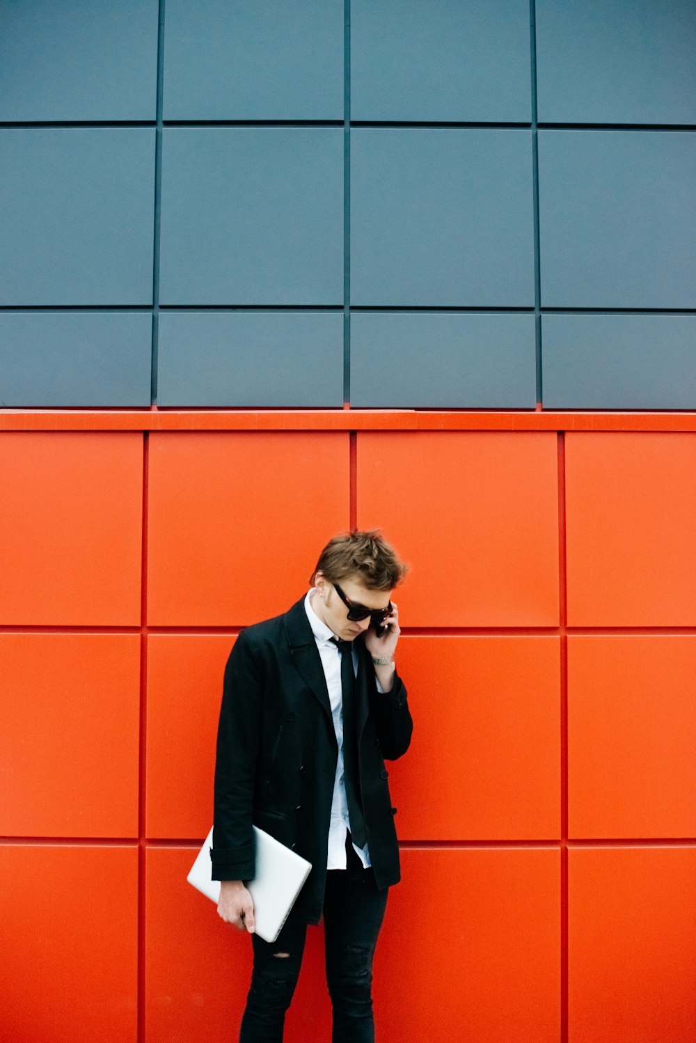 man in black blazer standing beside orange wall