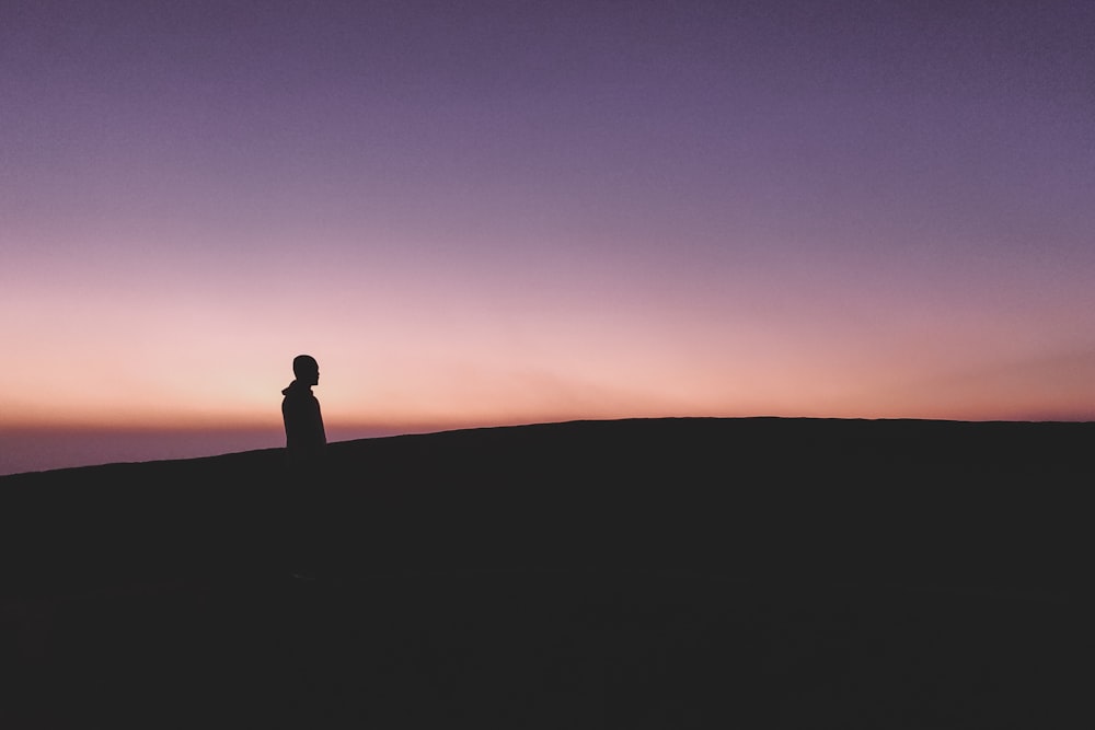 silhouette of man standing on rock during sunset