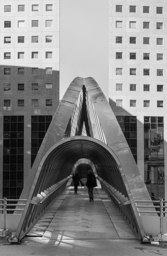 grayscale photo of man walking on bridge in La Défense France