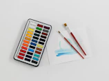 Close-up of watercolor paints arranged neatly with brushes resting beside them.