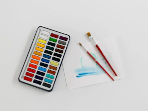 Close-up of watercolor paints arranged neatly with brushes resting beside them.
