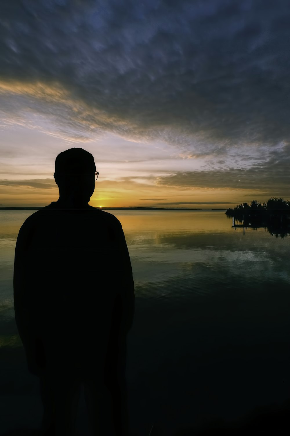 silhouette of man standing near body of water during sunset